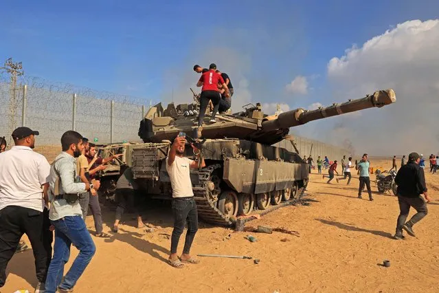 Palestinians take control of an Israeli tank after crossing the border fence with Israel from Khan Yunis in the southern Gaza Strip on October 7, 2023. Barrages of rockets were fired at Israel from the Gaza Strip at dawn as militants from the blockaded Palestinian enclave infiltrated Israel, with at least one person killed, the army and medics said. (Photo by Said Khatib/AFP Photo)