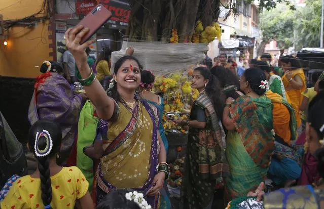 A Hindu woman takes a selfie as others perform rituals around a banyan tree on Vat Savitri festival in Mumbai, India, Thursday, June 24, 2021. Vat Savitri is celebrated on a full moon day where women pray for the longevity of their husbands. (Photo by Rafiq Maqbool/AP Photo)