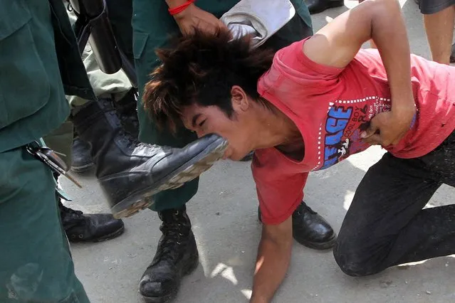 A Cambodian anti riot police officer kicks a protester (C) during a clash between police and garment workers in Phnom Penh on November 12, 2013. One woman was shot dead and several injured in violent clashes between protesting garment workers and riot police in the Cambodian capital on November 12, a rights group and family members said. (Photo by AFP Photo)