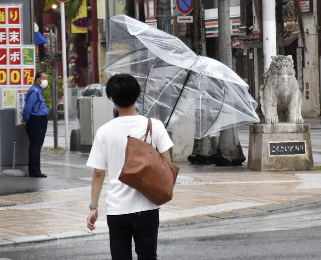 A man walks with an umbrella broken by strong winds in Naha, Okinawa, southern Japan, on Wednesday, July 21, 2021. A typhoon is forecast to bring heavy rains to Taiwan and coastal China over the weekend, days after the worst flooding on record in a central province. .(Photo by Kyodo News via AP Photo)