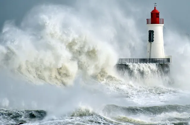 A waves breaks against a pier and a lighthouse in Les Sables-d'Olonne, western France, on February 9, 2016. High winds buffeted northwestern Europe on February 8, leaving one woman in France in a coma after she was hit by an advertising hoarding. Electricity was cut to 5,000 homes in northern France. (Photo by Loic Venance/AFP Photo)
