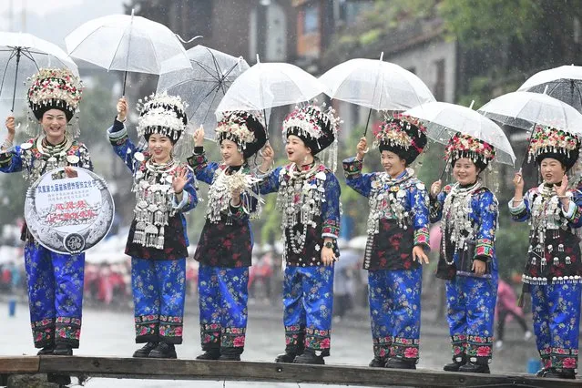 Miao women holding umbrellas stand on a wooden bridge to show traditional Miao costumes during a clothing culture festival at Fenghuang Ancient Town on November 10, 2023 in Xiangxi Tujia and Miao Autonomous Prefecture, Hunan Province of China. (Photo by Yang Huafeng/China News Service/VCG via Getty Images)