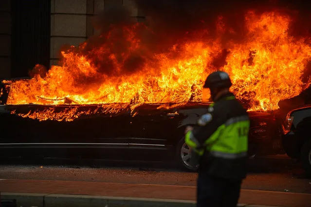 A Police officer stands near a car that was set on fire during protests near the inauguration of President Donald Trump in Washington, DC, U.S., January 20, 2017. (Photo by Bryan Woolston/Reuters)