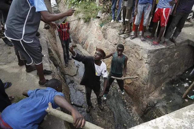 Demonstrators prepare to flush out Jean Claude Niyonzima a suspected member of the ruling party's Imbonerakure youth militia who escaped a lynching by escaping into a sewer in the Cibitoke district of Bujumbura, Burundi, Thursday May 7, 2015. (Photo by Jerome Delay/AP Photo)