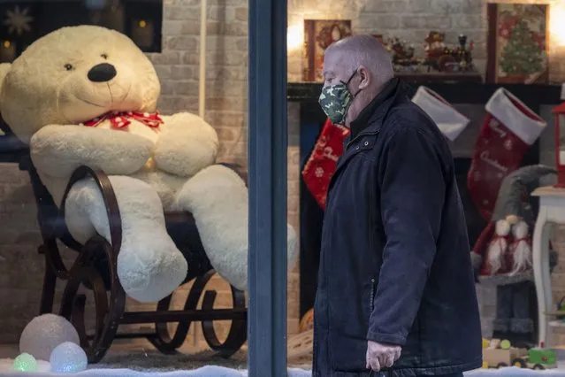 A man wears a face mask to curb the spread of coronavirus as he walks past a shop with Christmas decorations in Brussels, Belgium, Wednesday, November 17, 2021. Belgium reimposed an extended use of facemasks and mandatory remote work in an attempt to contain a new surge of COVID-19 cases. Prime Minister Alexander De Croo said that the use of facemasks indoors would be lowered to the x-plus age group and that remote work would be made mandatory for all for x days in the 5-day workweek until Christmas. (Photo by Olivier Matthys/AP Photo)