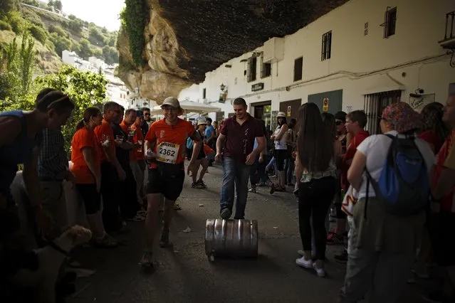 A waiter pushes a keg of beer while Spanish runner Javier Martin (L) sidesteps him as he participates in the XVIII 101km international competition in Setenil de las Bodegas, southern Spain, May 9, 2015. (Photo by Jon Nazca/Reuters)