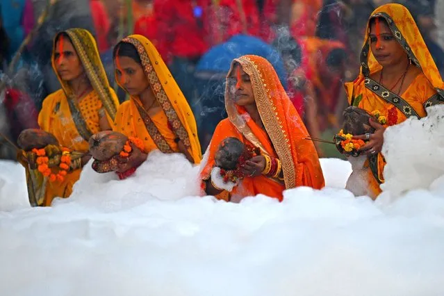 Devotees perform religious rituals as they offer prayers to Sun god while standing in the waters of river Yamuna coated with polluted foam on the occasion of the Hindu festival of Chhat Puja in Noida on November 10, 2021. (Photo by Money Sharma/AFP Photo)