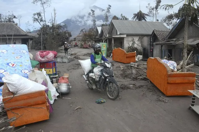 A man carries his belongings on a motorbike through furniture waiting outside homes for evacuation at a village affected by the eruption of Mount Semeru, in Supiturang village, Lumajang, East Java, Indonesia, Tuesday, December 7, 2021. Indonesia's president on Tuesday visited areas devastated by a powerful volcanic eruption that killed a number of people and left thousands homeless, and vowed that communities would be quickly rebuilt. (Photo by Hendra Permana/AP Photo)