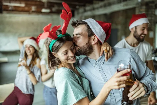Young loving couple having fun while spending New Year's party at casual office. Man is kissing woman. (Photo by skynesher/Getty Images)