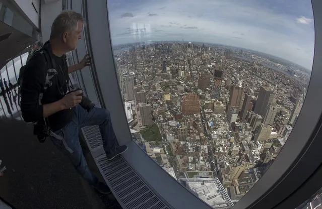 A news photographer looks out the window at the Manhattan skyline from the One World Observatory observation deck on the 100th floor of the One World Trade center tower in New York during a press tour of the site May 20, 2015. (Photo by Mike Segar/Reuters)