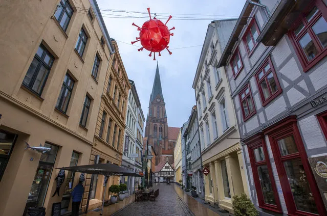 A homemade, luminous representation of the coronavirus hangs above a shopping street in front of the tower of Schwerin Cathedral during the lockdown in Schwerin, Germany, Tuesday, January 5, 2021. A local fishmonger in the almost deserted street built and hung the lantern in the image of the virus. The German Chancellor and the Minister Presidents of the federal states discuss an extension of the lockdown to contain the corona pandemic. (Photo by Jens Buettner/dpa via AP Photo)
