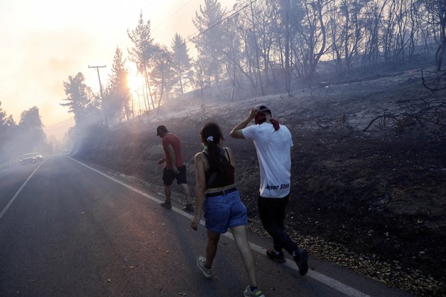 Residents walk to their homes, in an area affected by a wildfire, that burned parts of rural areas in Quillon, Chile on February 2, 2023. (Photo by Juan Gonzalez/Reuters)