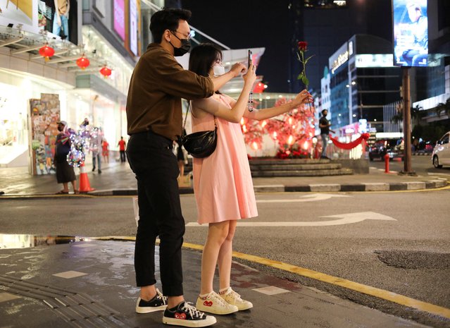 A couple wearing protective masks take a picture of a rose on Valentine's Day in Kuala Lumpur, Malaysia on February 14, 2022. (Photo by Hasnoor Hussain/Reuters)