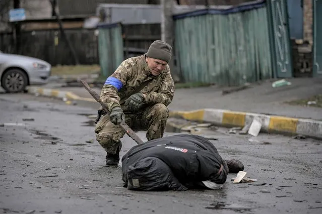 A Ukrainian serviceman uses a piece of wood to check if the body of a man dressed in civilian clothing is booby-trapped with explosive devices, in the formerly Russian-occupied Kyiv suburb of Bucha, Ukraine, Saturday, April 2, 2022. As Russian forces pull back from Ukraine's capital region, retreating troops are creating a “catastrophic” situation for civilians by leaving mines around homes, abandoned equipment and “even the bodies of those killed”, President Volodymyr Zelenskyy warned Saturday. (Photo by Vadim Ghirda/AP Photo)