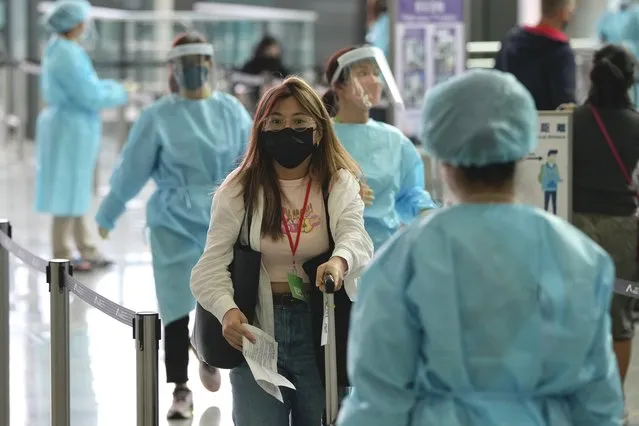 Workers wearing gowns, masks and gloves, direct arriving passengers from Manila for buses to quarantine hotels in Hong Kong international airport, Friday, April 1, 2022. The first flight to arrive in Hong Kong after authorities lifted a COVID ban on arrivals from nine countries including Australia, Canada, France, India, Nepal, Pakistan, the Philippines, the UK and the US. (Photo by Kin Cheung/AP Photo)