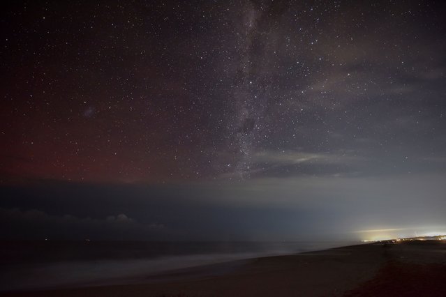 The Aurora Australis, also known as the Southern Lights, is faintly seen over the Atlantic Ocean to the left of the Milky Way from Santa Monica beach near Jose Ignacio, Maldonado Department, Uruguay, on May 11, 2024, with the lights of Punta del Este glowing on the right. The most powerful solar storm in more than two decades struck Earth, triggering spectacular celestial light shows from Tasmania to Britain – and threatening possible disruptions to satellites and power grids as it persists into the weekend. (Photo by Mariana Suarez/AFP Photo)