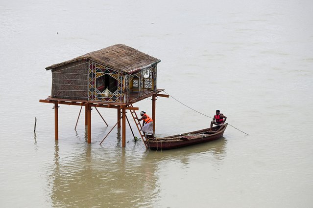 Men row a boat near a deluged straw hut in the river Ganges in Prayagraj on August 7, 2024, after rise in water levels during the monsoons. (Photo by Sanjay Kanojia/AFP Photo)