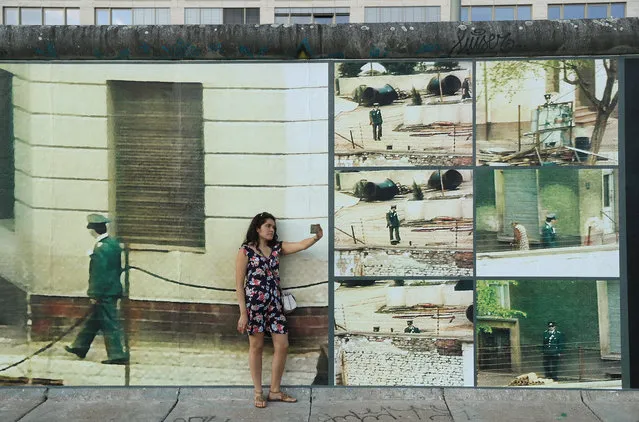 A young woman from Peru shoots a selfie in front of a portion of the art installation “Beyond The Wall” by German-American artist Stefan Roloff at a section of the former Berlin Wall called the East Side Gallery on August 14, 2017 in Berlin, Germany. The installation, which will be up from August 13 through November 9, combines images from the Berlin Wall during the Cold War with the accounts of people persecuted by the East German secret police. (Photo by Sean Gallup/Getty Images)