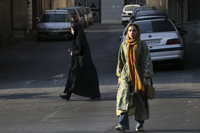 In this Thursday, August 24, 2017, photo, two Iranian women make their way in a square while one of them wears the chador in downtown Tehran, Iran. She is just a couple of weeks into her appointment as new Iranian vice president but Laaya Joneidi's decision to abandon her headscarf and fashion style for the all-encompassing black chador is raising questions among women in the Islamic Republic – especially after she said that President Hassan Rouhani personally asked her to wear the more conservative Muslim women's garment. (Photo by Vahid Salemi/AP Photo)