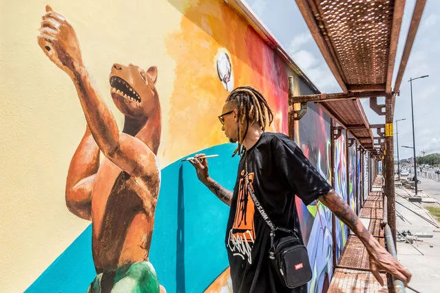 Brazilian artist Dos Santos Edgar Bernado, also known as Ed-mun, paints with a brush at the Effet Graff festival, whose objective is to achieve one of the longest murals in the world, in Cotonou on May 18, 2022. 26 Beninese and international graffiti artists are taking part in the eighth edition of the Effet Graff festival in Cotonou, with the ambition of creating one of the largest murals in the world that traces the history and culture of Benin. The fresco pays tribute in particular to the 26 Beninese treasures looted by French colonial troops and returned to Benin in November 2021, and the theme of this edition is a “new Benin”. (Photo by Yanick Folly/AFP Photo)