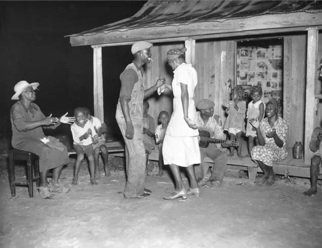 After a long day of picking cotton, people enjoy music and dance at night outside a cabin on August 31, 1937.  These workers are among 700 blacks living on the Will Howard Smith plantation near Prattville, Alabama. (Photo by AP Photo)