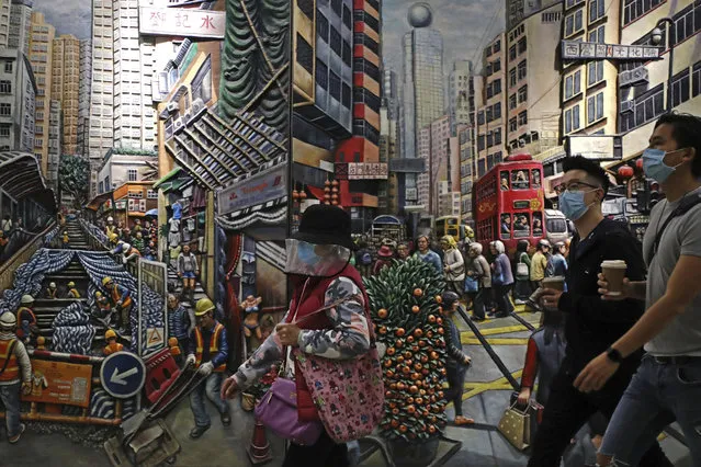 People wearing face masks to protect themselves from possibly contracting the coronavirus COVID-19 as they walk past a painting in Hong Kong, Saturday, April 25, 2020. (Photo by Kin Cheung/AP Photo)