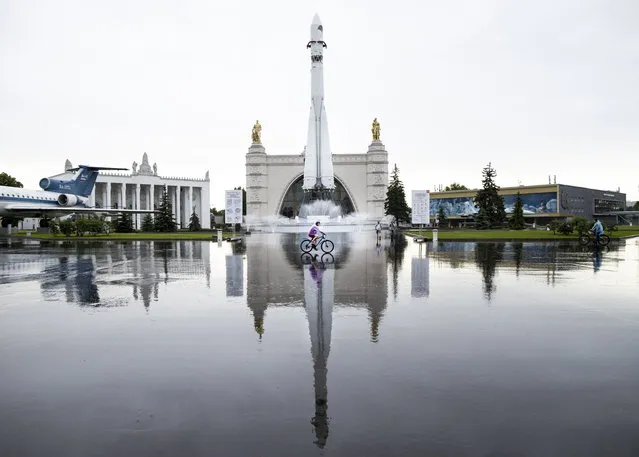 A girl rides a bicycle in front of a fountain and Cosmos pavilion with a Soviet era Vostok rocket, at the VDNKh, the All-Russia Exhibition of National Economy, during rain in Moscow, Russia, Wednesday, June 10, 2020. Moscow fountains opened Wednesday, a day after the city lifted a lockdown intended to stem the coronavirus outbreak. (Photo by Alexander Zemlianichenko/AP Photo)
