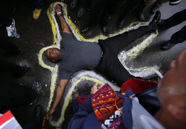 A protestor lies on the ground with a chalk outline marking his position during a demonstration at the Ferguson Police Department in Ferguson, Missouri, October 13, 2014. Hundreds of protesters converged in the pouring rain on the Ferguson, Missouri, police department on Monday as they launched another day of demonstrations over the August killing by police of an unarmed black teenager. (Photo by Jim Young/Reuters)