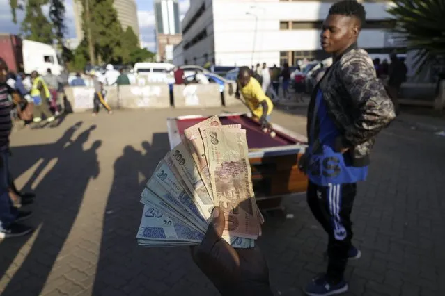A person holds banknotes as people play pool in an open space in Harare, Zimbabwe, Wednesday, November 30, 2022. Previously a minority and elite sport in Zimbabwe, the game has increased in popularity over the years, first as a pastime and now as a survival mode for many in a country where employment is hard to come by. (Photo by Tsvangirayi Mukwazhi/AP Photo)