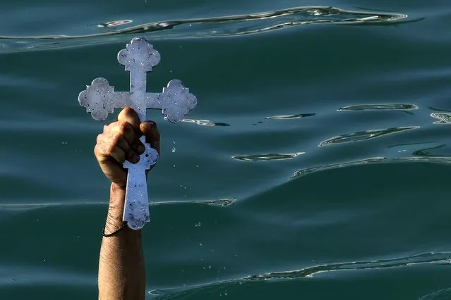 A pilgrim holds up the cross after it was thrown by an Orthodox priest into the water, during an epiphany ceremony to bless the sea, on the southeast resort of Ayia Napa, Cyprus, Friday, January 6, 2023. By tradition, a crucifix is cast into the waters of a lake or river, and it is believed that the person who retrieves it will be freed from evil spirits and will be healthy through the year. (Photo by Petros Karadjias/AP Photo)