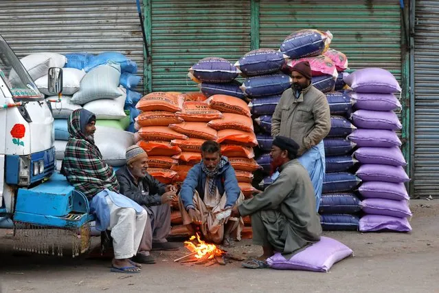 Labourers keep themselves warm near a fire during a cold morning, as they wait for work at the wholesale grain market in Karachi, Pakistan on January 23, 2023. (Photo by Akhtar Soomro/Reuters)