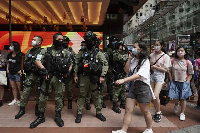 Pedestrians pass police standing guard during China's National Day in Causeway Bay, Hong Kong, Thursday, October 1, 2020. A popular shopping district in Causeway Bay saw a heavy police presence the Oct. 1  National Day holiday despite low protester turnout. (Photo by Kin Cheung/AP Photo)