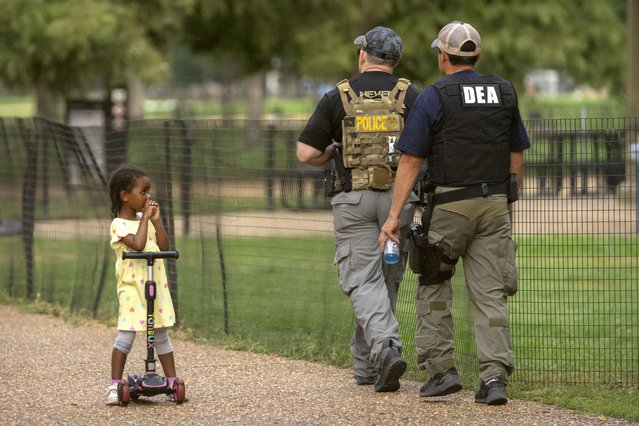 A child watches as officers with the Drug Enforcement Administration patrol along the National Mall Wednesday, August 13, 2025, in Washington. (Photo by Mark Schiefelbein/AP Photo)