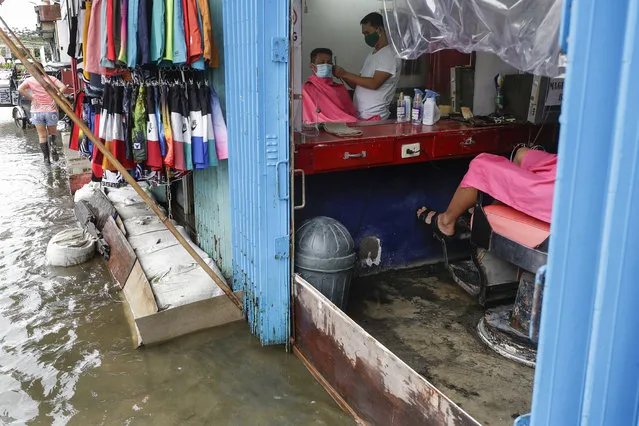 A man has his hair cut at a barbershop flooded by Typhoon Molave in Pampanga province, northern Philippines on Monday, October 26, 2020. The fast moving typhoon has forced thousands of villagers to flee to safety in provinces. (Photo by Aaron Favila/AP Photo)