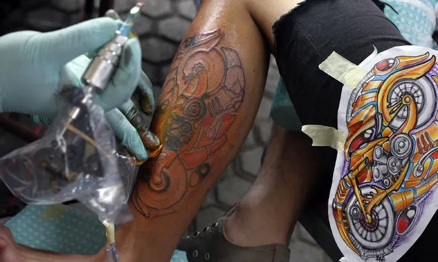 A tattoo artist creates tattoo on a leg of visitor during Bandung Body Art Festival at in Bandung, West Java, on December 7, 2014. (Photo by Rezza Estily/JG Photo)