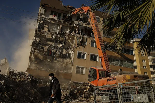 A worker walks past as others demolish a building that was damaged at the Oct. 30 earthquake in Izmir, Turkey, Wednesday, November 4, 2020. Search and rescue operations for survivors had been completed Wednesday at several buildings that fell in the coastal city. More that a hundred people were killed and more that a thousand people were injured. (Photo by Emrah Gurel/AP Photo)
