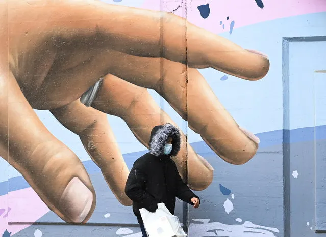 A man wearing a protective mask walks past a mural during the COVID-19 pandemic in Toronto on Tuesday, December 1, 2020. Toronto and Peel region continue to be in lockdown. (Photo by Nathan Denette/The Canadian Press via AP Photo)
