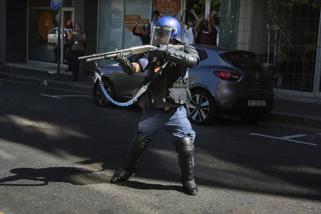A member of the South African riot police aims his shotgun to disperse students supporting the “Fees Must Fall movement” protest outside the South African Parliament where South African Minster of Finance delivers his Mid- term Budget address in Cape Town, on October 26, 2016 Weeks of protests at South African universities have targeted tuition fees – but students say they are also about racism and inequality in a society still plagued by the legacy of apartheid. (Photo by Rodger Bosch/AFP Photo)