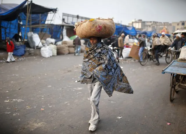 A vendor wrapped in a shawl carries flowers for sale at a market place on a cold winter morning in the old quarters of Delhi December 31, 2014. (Photo by Ahmad Masood/Reuters)