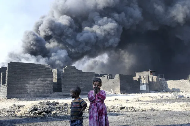 Children are seen at the street as smoke rise from oil wells, were set on fire by Daesh terrorists to limit coalition forces pilots' eyesight and to make the wells out o service following Iraqi army's retaking of Al Qayyarah town from Daesh during the operation to retake Iraq's Mosul from Daesh, in Mosul, Iraq on October 25, 2016. Black smoke affects human life in town badly. (Photo by Emrah Yorulmaz/Anadolu Agency/Getty Images)