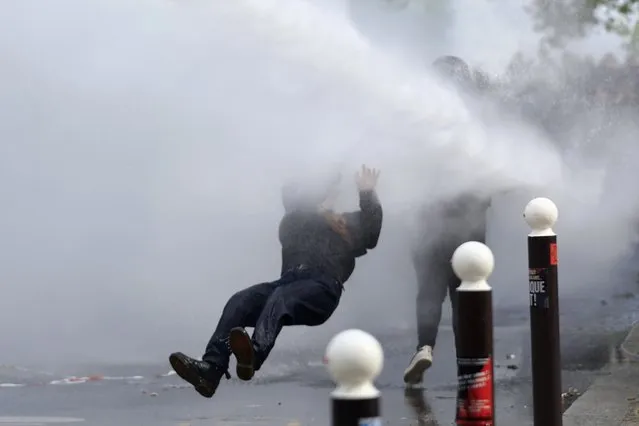 A protester is overthrown as police forces use water canon during a demonstration, Monday, May 1, 2023 in Paris. Across France, thousands marched in what unions hope are the country's biggest May Day demonstrations in years, mobilized against President Emmanuel Macron's recent move to raise the retirement age from 62 to 64. (Photo by Aurelien Morissard/AP Photo)