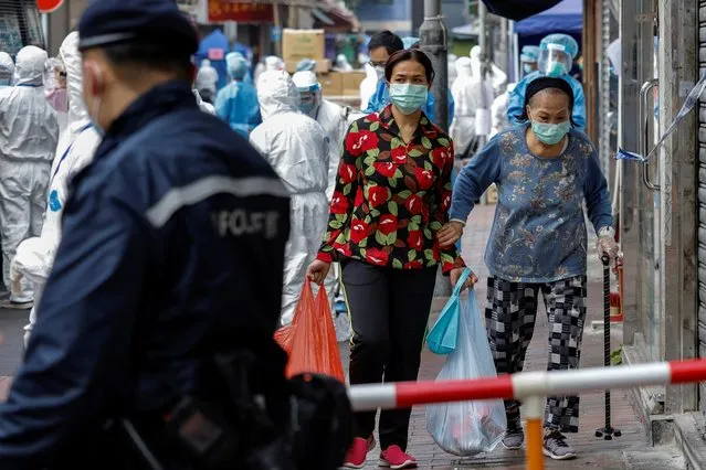 Residents carry bags of grocery inside a locked down portion of the Jordan residential area to contain a new outbreak of the coronavirus disease (COVID-19), in Hong Kong, China on January 23, 2021. (Photo by Tyrone Siu/Reuters)