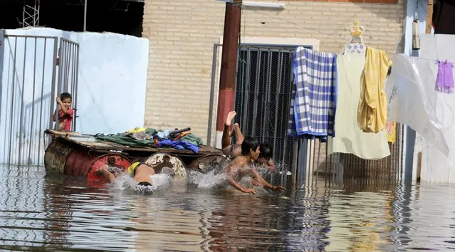 Children bathe near houses that are partially submerged in flood waters in Asuncion, December 20, 2015. (Photo by Jorge Adorno/Reuters)
