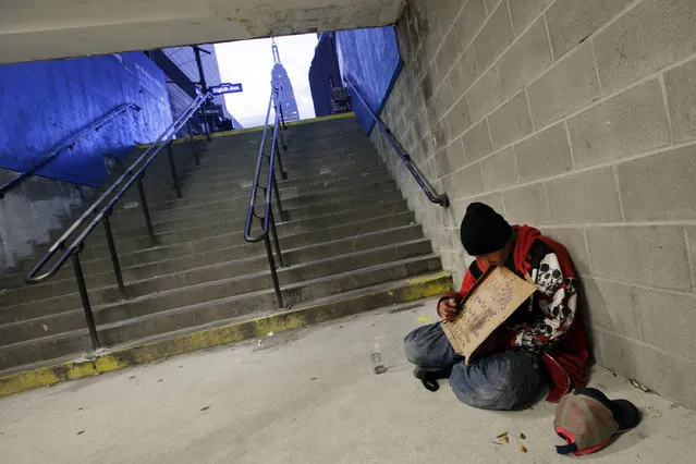 In this October 9, 2015 file photo, a homeless man holds a sign asking for money while sitting at the entrance to a subway station in New York. New York City plans to deploy hundreds of outreach workers who will canvass much of Manhattan every day with a deceptively simple goal: talk to as many homeless people as possible, as often as possible.  (Photo by Mark Lennihan/AP Photo)