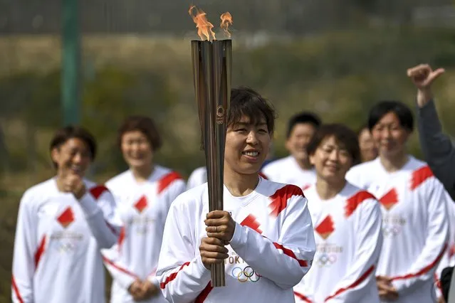 Japanese torchbearer Azusa Iwashimizu, center, a member of Japan women's national football team, arrives at a torch kiss point to pass on the flame during the torch relay grand start outside J-Village National Training Center in Naraha, Fukushima prefecture, northeastern Japan, Thursday, March 25, 2021. The torch relay for the postponed Tokyo Olympics began its 121-day journey across Japan on Thursday and is headed toward the opening ceremony in Tokyo on July 23. (Photo by Philip Fong/Pool Photo via AP Photo)