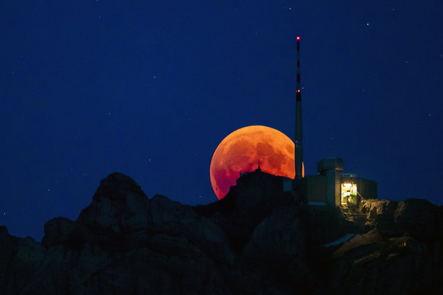 The moon turns red during a total lunar eclipse, behind the Saentis in Luzern, Switzerland, Friday, July 27, 2018. Skywatchers around much of the world are looking forward to a complete lunar eclipse that will be the longest this century. (Photo by Christian Merz/Keystone via AP Photo)