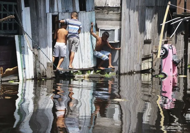 Children play outside a house, surrounded by the floodwaters of the Negro River in Manaus, Brazil, Thursday, May 20, 2021. According to official records taken by the Port of Manaus, the city is facing one of its worse floods in years, with levels not seen since 1902, making it the second-worst flood ever recorded. (Photo by Edmar Barros/AP Photo)