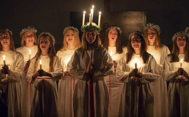 Young women sing carols as they hold candles to celebrate St. Lucia's Day in the Evangelical Lutheran Church of Saint Katarina in St.Petersburg, Russia, Thursday, December 13, 2018. The Church was built in the 19th century by and for Swedish expatriates in Saint Petersburg, and it is usually called the Swedish church. In Soviet era the Church used as a sport hall. St. Lucia is the patron saint of vision. (Photo by Dmitri Lovetsky/AP Photo)