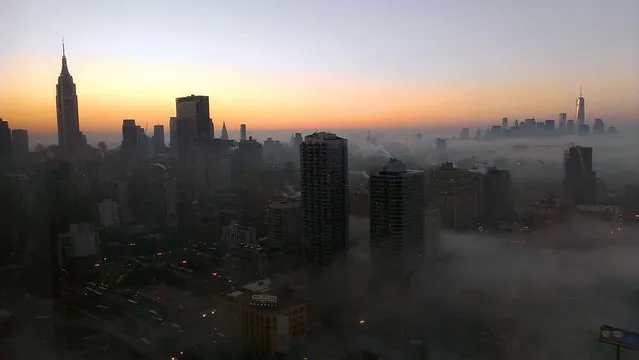 The tower of New York's World Trade Center, right, rises through a blanket of fog on Wednesday morning, Jan. 15, 2014, in this view looking south from the 48th floor at 42nd St. and 11th Ave in Midtown Manhattan. The Empire State Building is visible at left. (Photo by Girish Tewani/AP Photo)