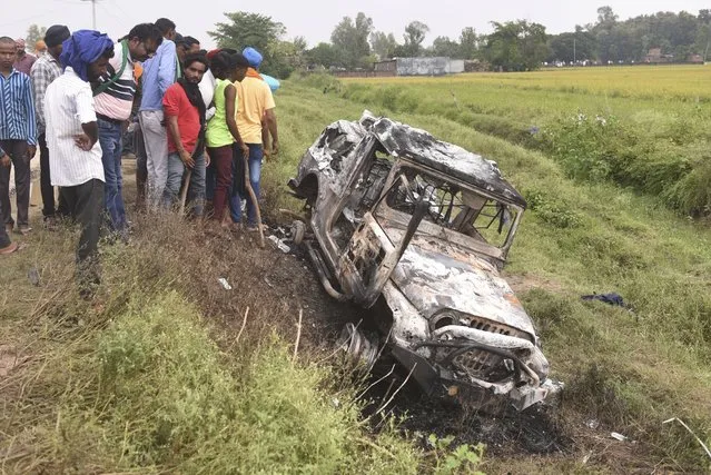 Villagers watch a burnt car which ran over and killed farmers on Sunday, at Tikonia village in Lakhimpur Kheri, Uttar Pradesh state, India, Monday, October 4, 2021. Indian police on Saturday, Oct. 9, arrested the son of a junior minister in Prime Minister Narendra Modi’s government as a suspect days after nine people were killed in a deadly escalation of yearlong demonstrations by tens of thousands of farmers against contentious agriculture laws in northern India, a police officer said. (Photo by AP Photo/Stringer)